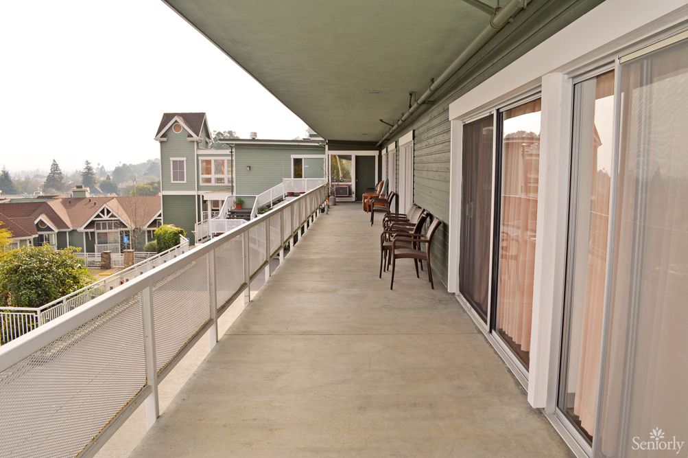 A long outdoor corridor with seating at an apartment building.