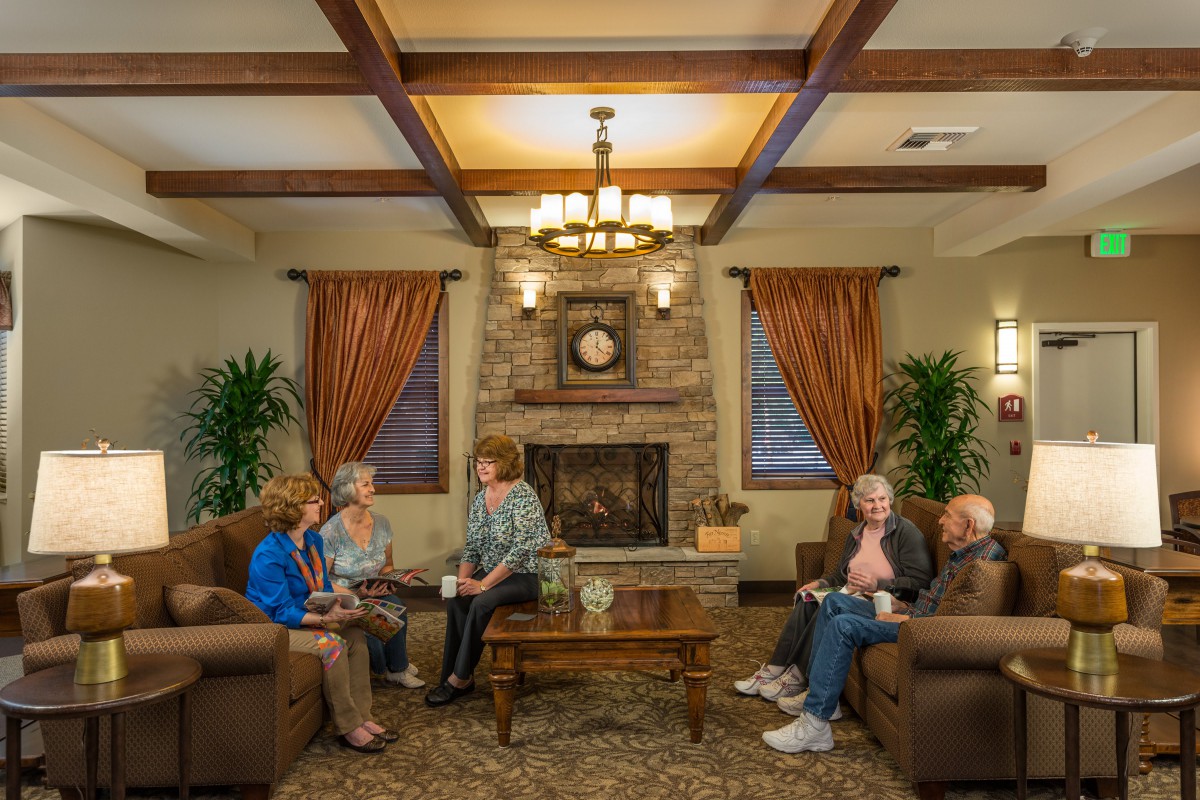A cozy living room with seniors engaging in conversation around a coffee table by the fireplace.