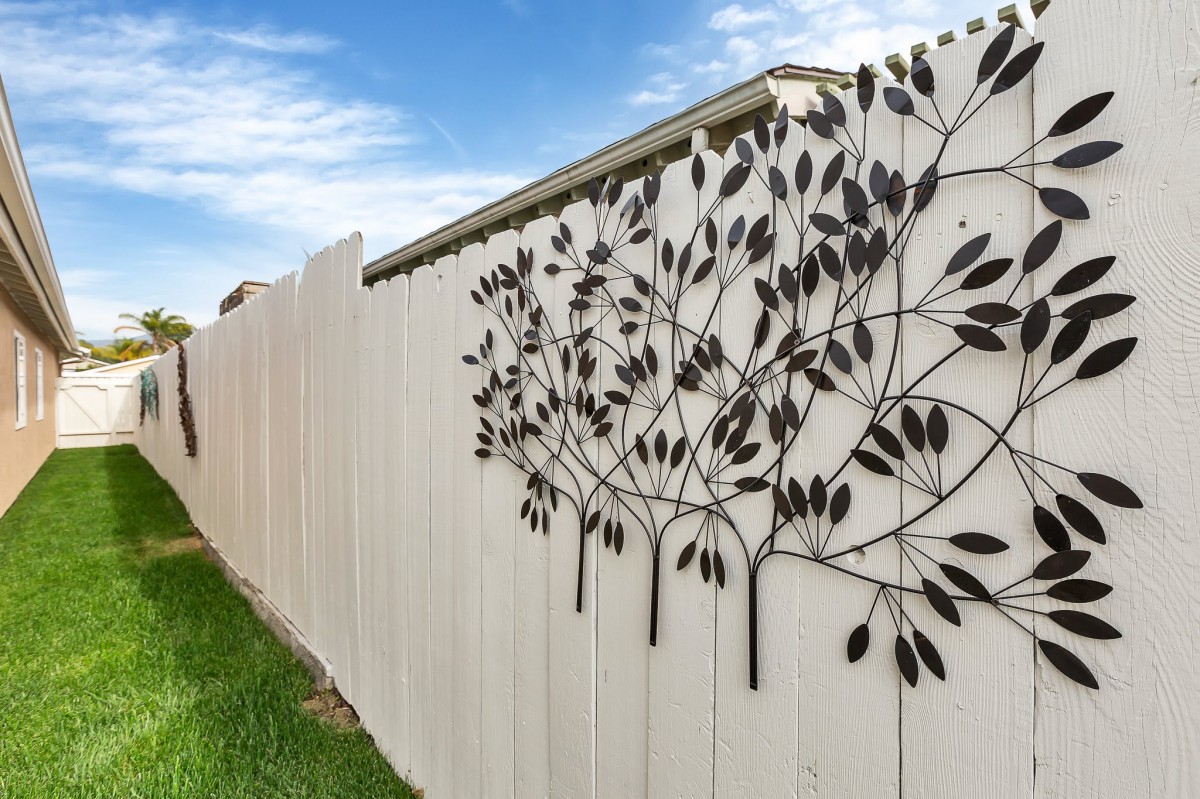 A white fence featuring decorative metal art with a leaf design.