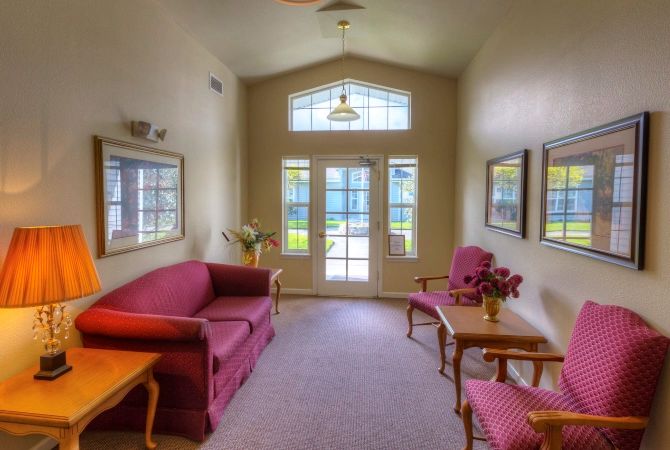 A cozy living room with sofas and a coffee table, featuring large windows and a doorway leading outside.