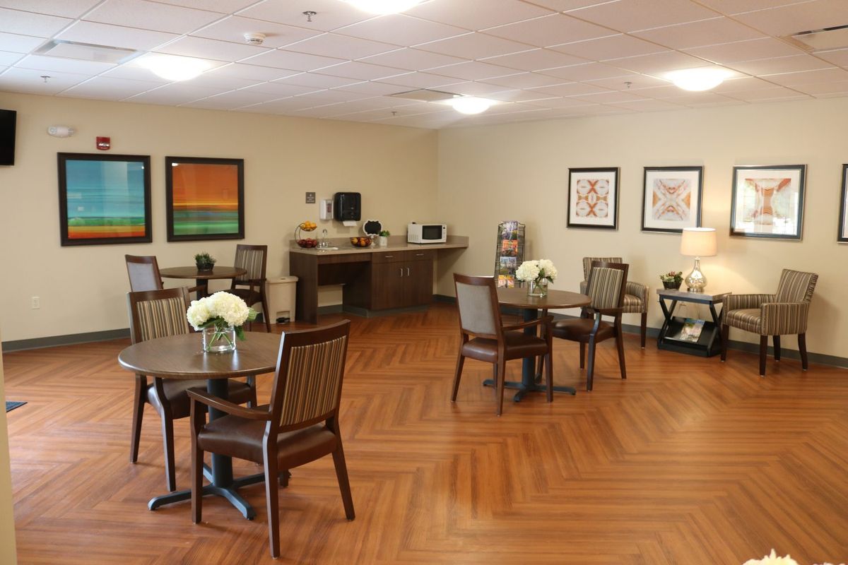 A cozy dining area with wooden tables and chairs, decorated with flowers and artwork on the walls.