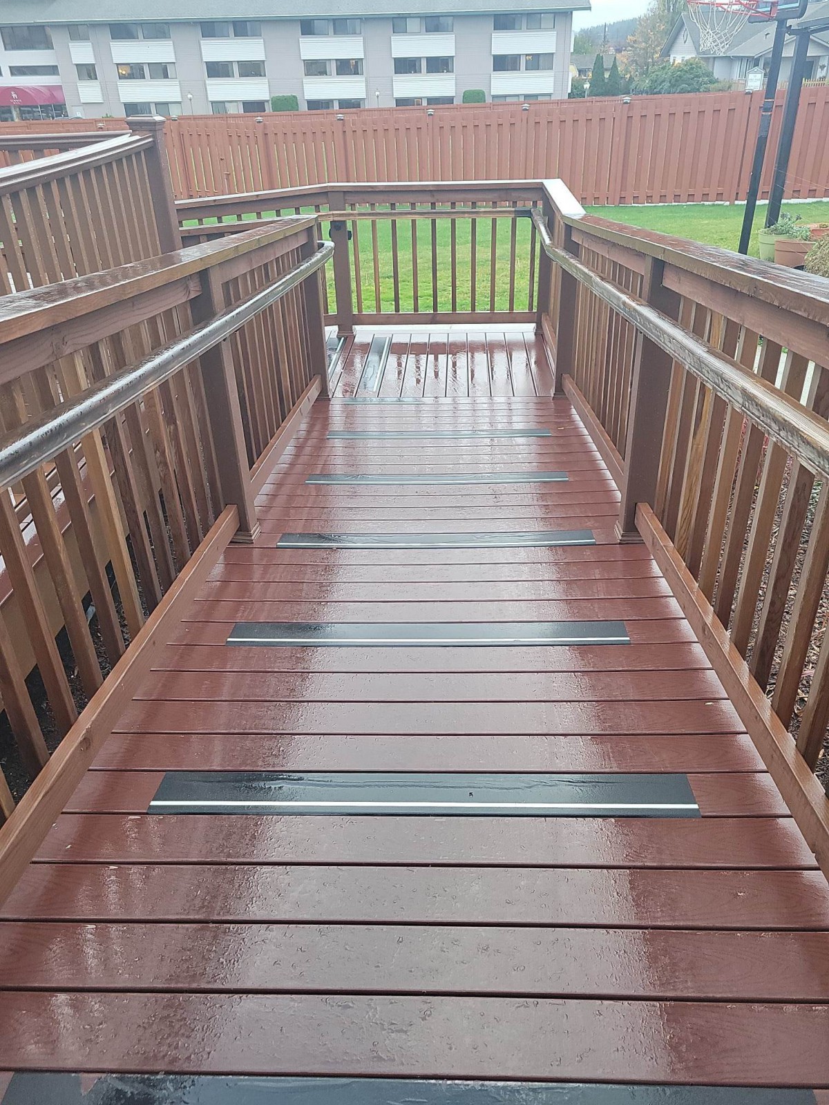 A wooden ramp with handrails, featuring a wet surface after rain.