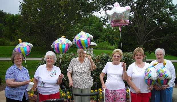 A group of elderly women celebrating outdoors with colorful balloons.