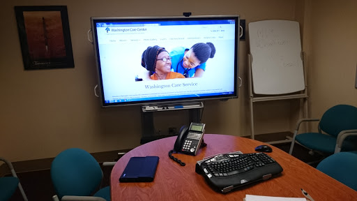 An office meeting room featuring a large screen display, a phone, and a keyboard on the table.