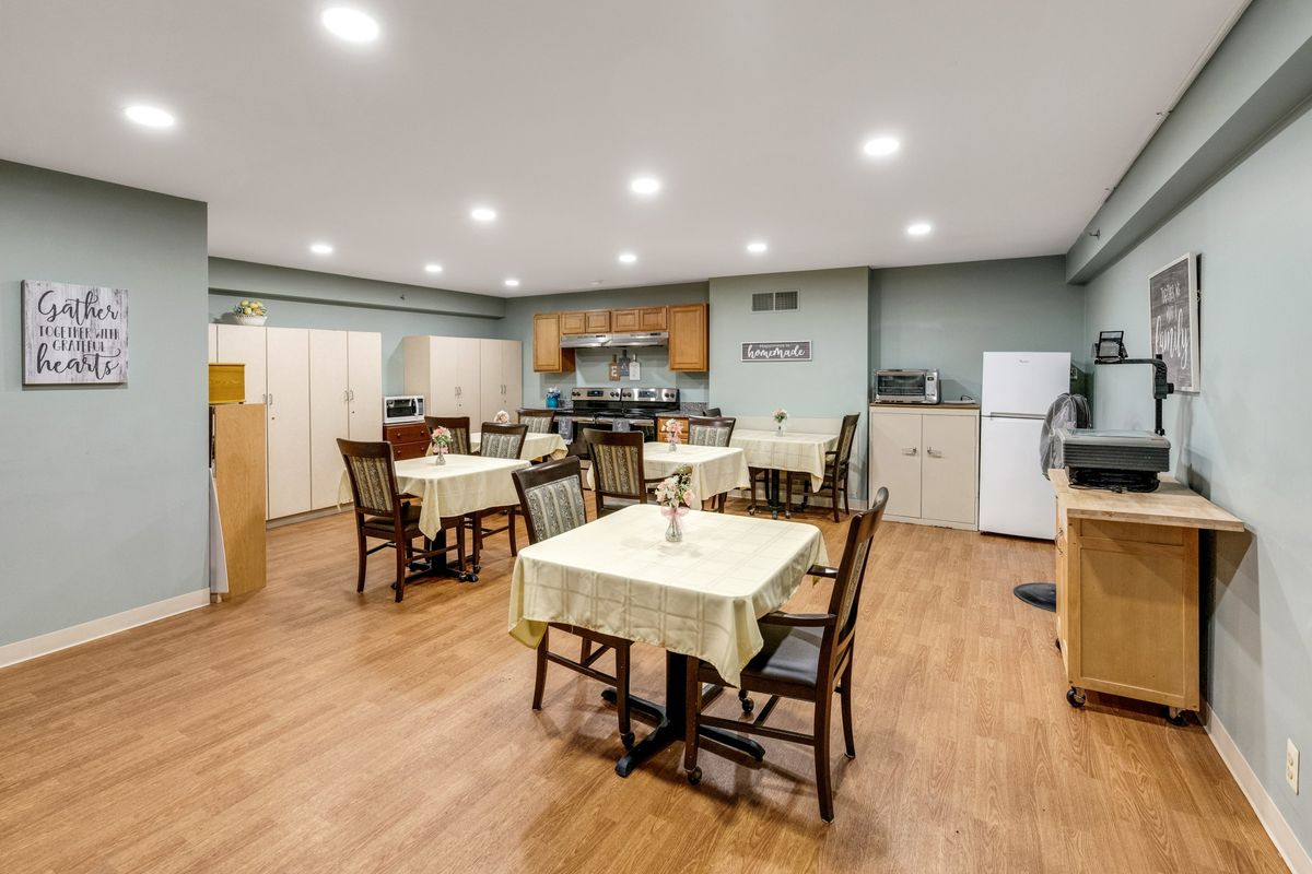 A spacious dining area with multiple tables and chairs, featuring a kitchen in the background.