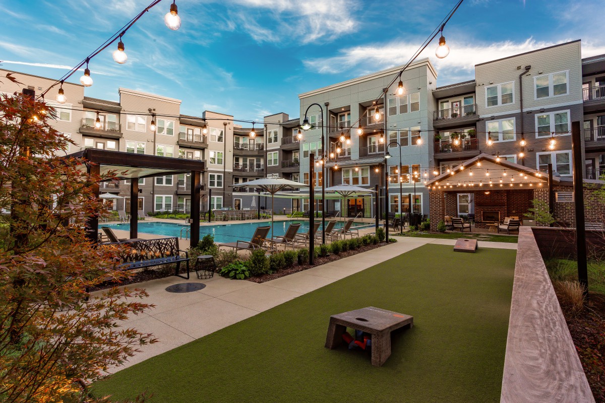 Modern apartment complex with a courtyard featuring a swimming pool and ambient string lighting.