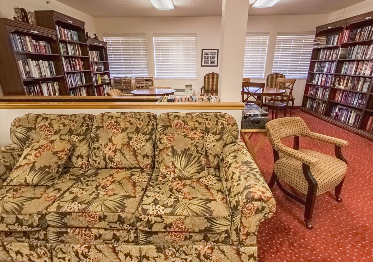A cozy library space with floral patterned sofas, carpeted floor, and bookshelves lining the walls.