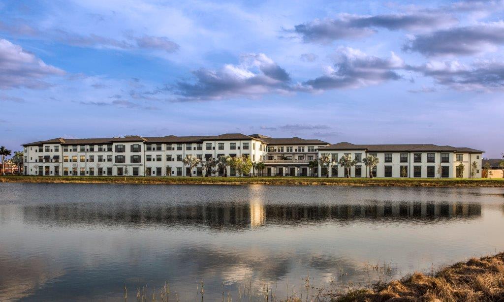 A large building with its reflection mirrored in a calm lake under a cloudy sky.