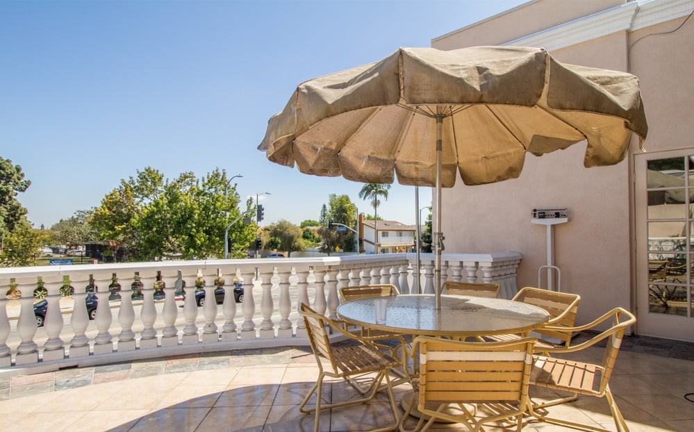 A sunny patio with a table, chairs, and an umbrella overlooking a balcony.