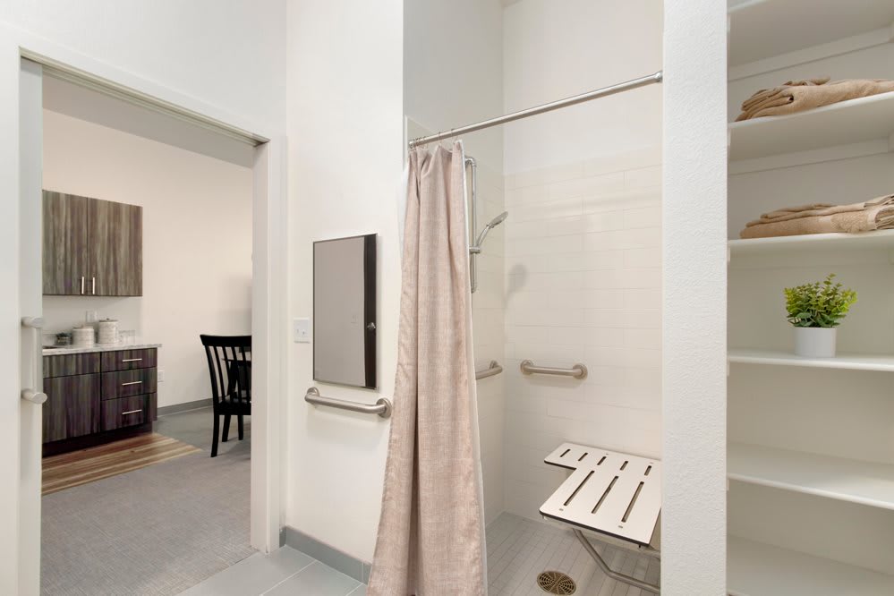 A modern accessible bathroom with a walk-in shower featuring a bench seat and grab bars.