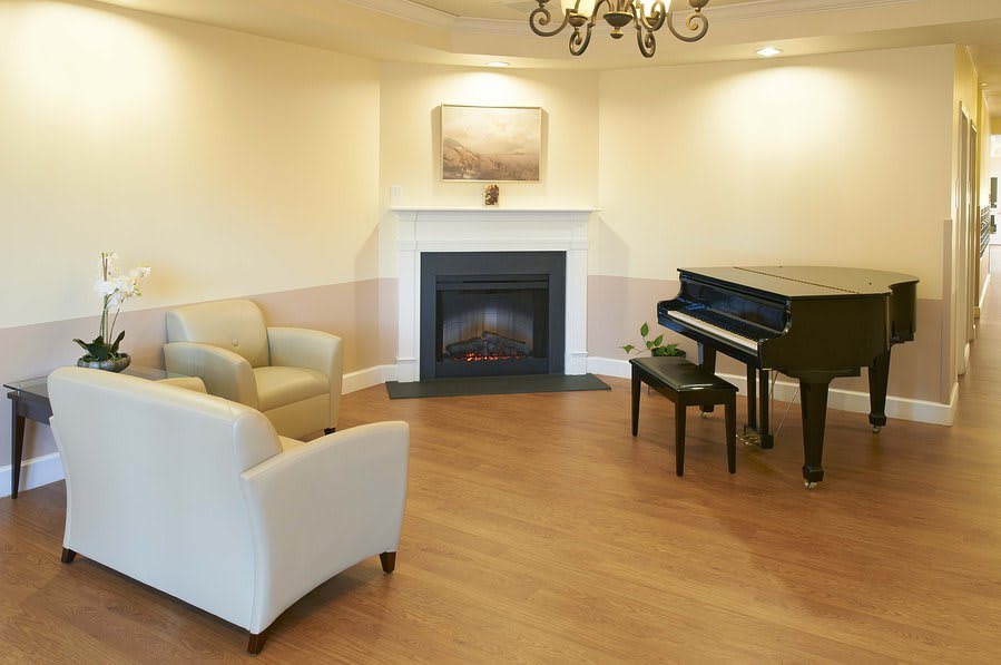 A cozy living room featuring a grand piano and a warm fireplace, complemented by comfortable seating.