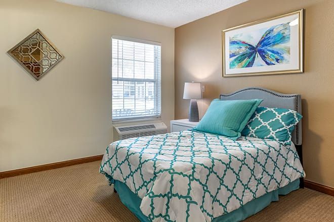 A cozy bedroom with teal and white bedding, a bedside lamp, and butterfly artwork on the wall.