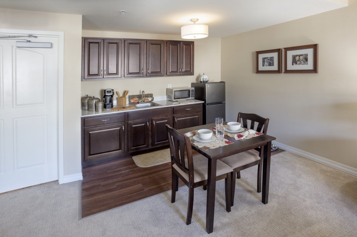 A compact kitchen with dark wooden cabinets and a small dining area featuring a table set for two.