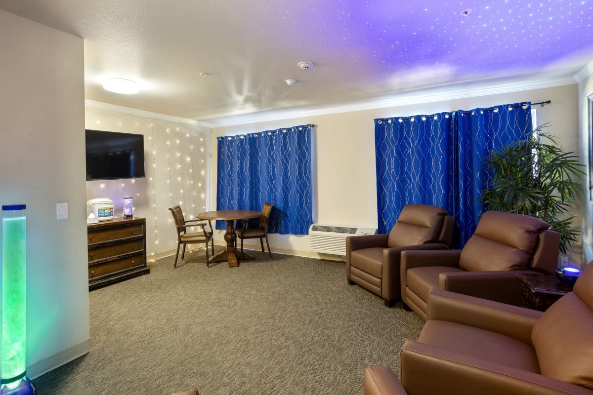A cozy living room with comfortable chairs, a television, and a small dining table under soft indoor lighting.