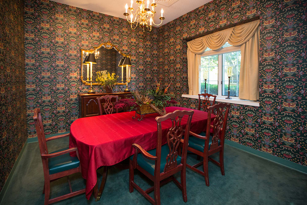 A vintage-style dining room featuring a red tablecloth, ornate wallpaper, and a classic chandelier.