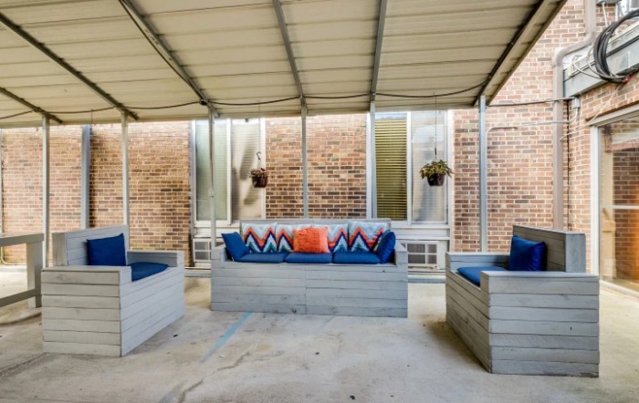 A cozy patio with cushioned seating under a canopy, decorated with colorful pillows and hanging plants.