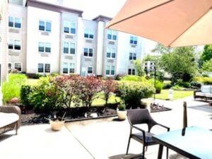 A sunny patio area with chairs and a table under an umbrella, overlooking a garden and modern building.