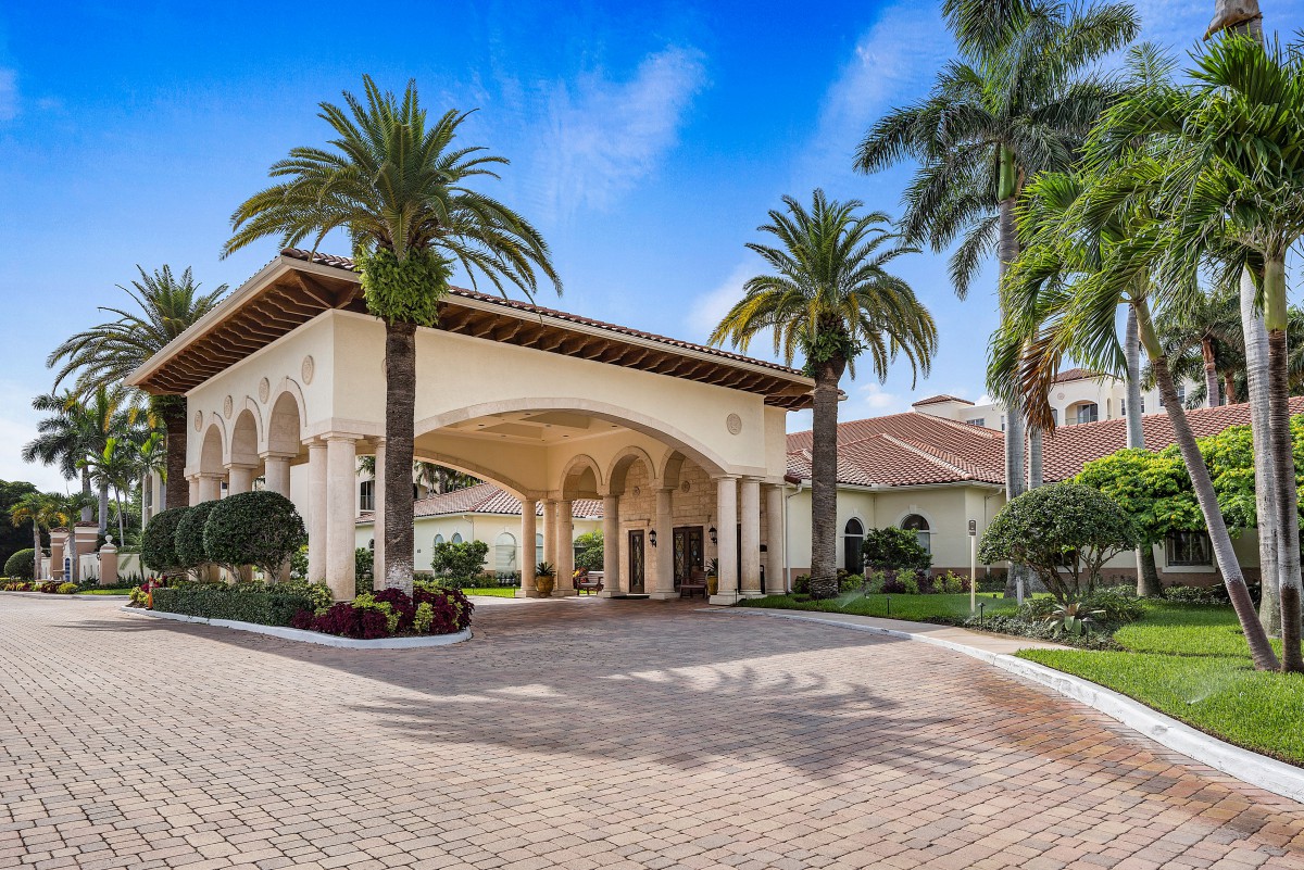 A luxurious tropical residence with a grand driveway and palm trees.