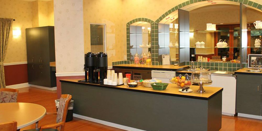 A kitchen area with a coffee station and breakfast bar, featuring various beverages and fresh fruit on the counter.