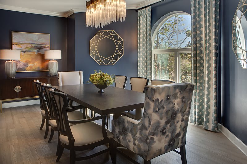 A modern dining room with blue walls, featuring elegant furniture, a chandelier, and a decorative mirror.