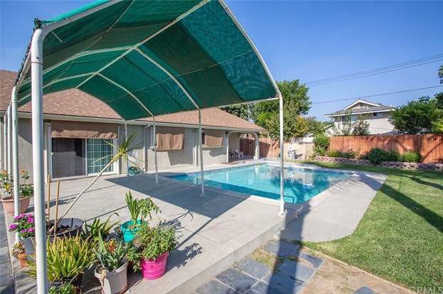 A backyard with a swimming pool, shaded seating area, and potted plants.