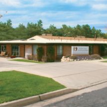 A small clinic building with a parking area and landscaped surroundings.