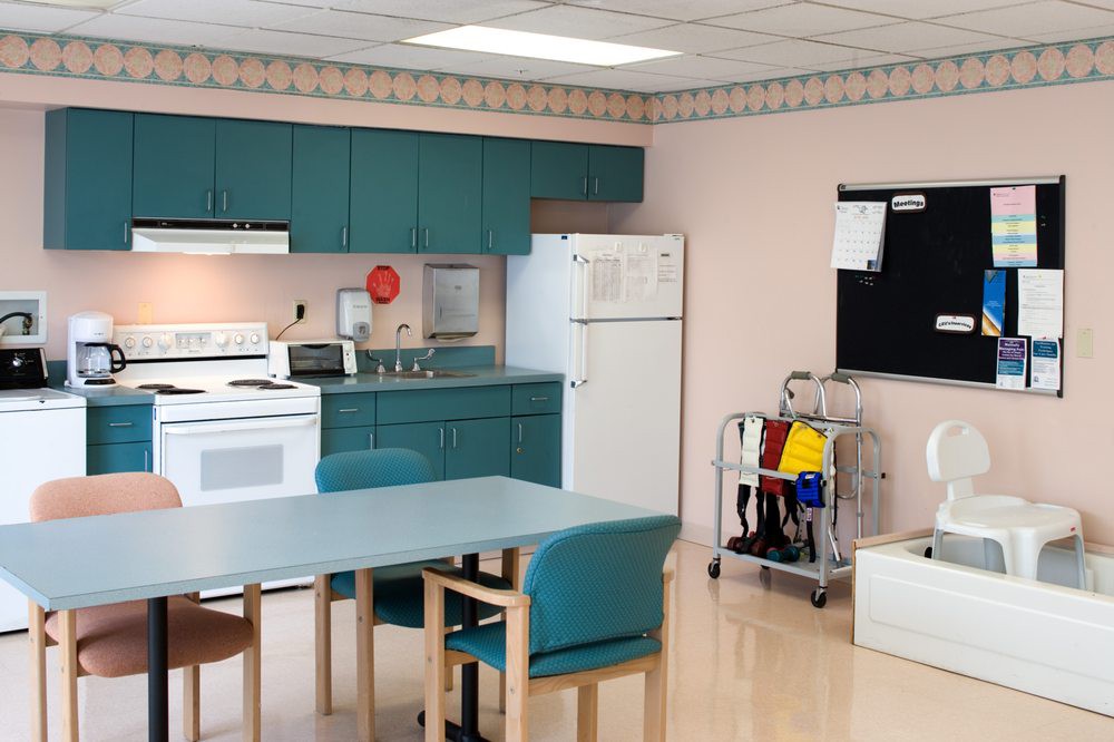 A kitchen with teal cabinets, dining table, and chairs alongside a refrigerator and stove.