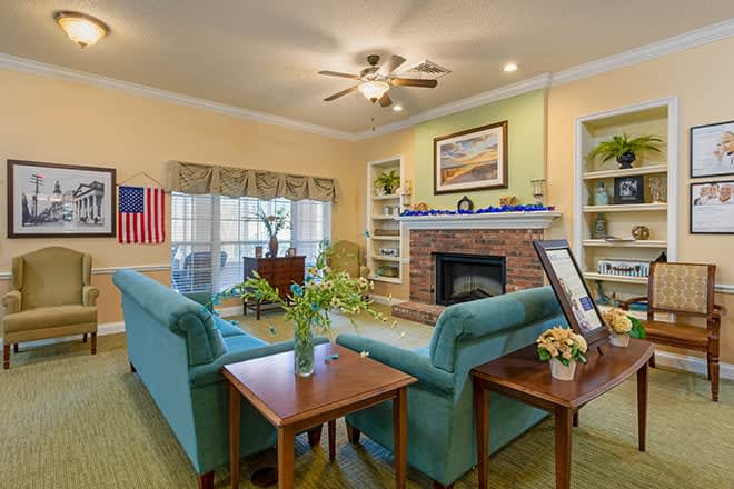 A cozy living room featuring teal sofas, a central fireplace, and a ceiling fan, with an American flag displayed on the wall.