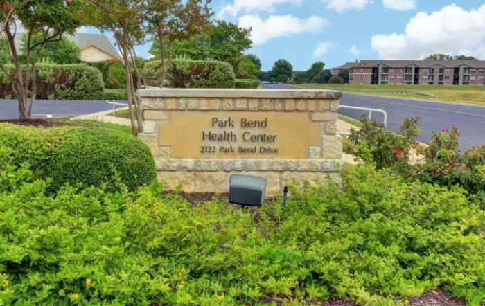 Stone sign for Park Bend Health Center surrounded by greenery.