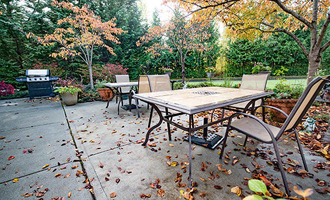 A cozy outdoor patio area with a table and chairs surrounded by autumn foliage.