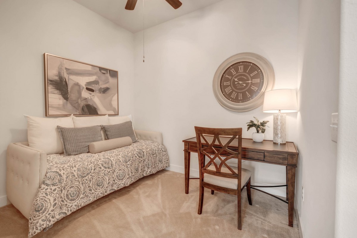A cozy bedroom featuring a daybed, a desk with a lamp, and elegant wall art.