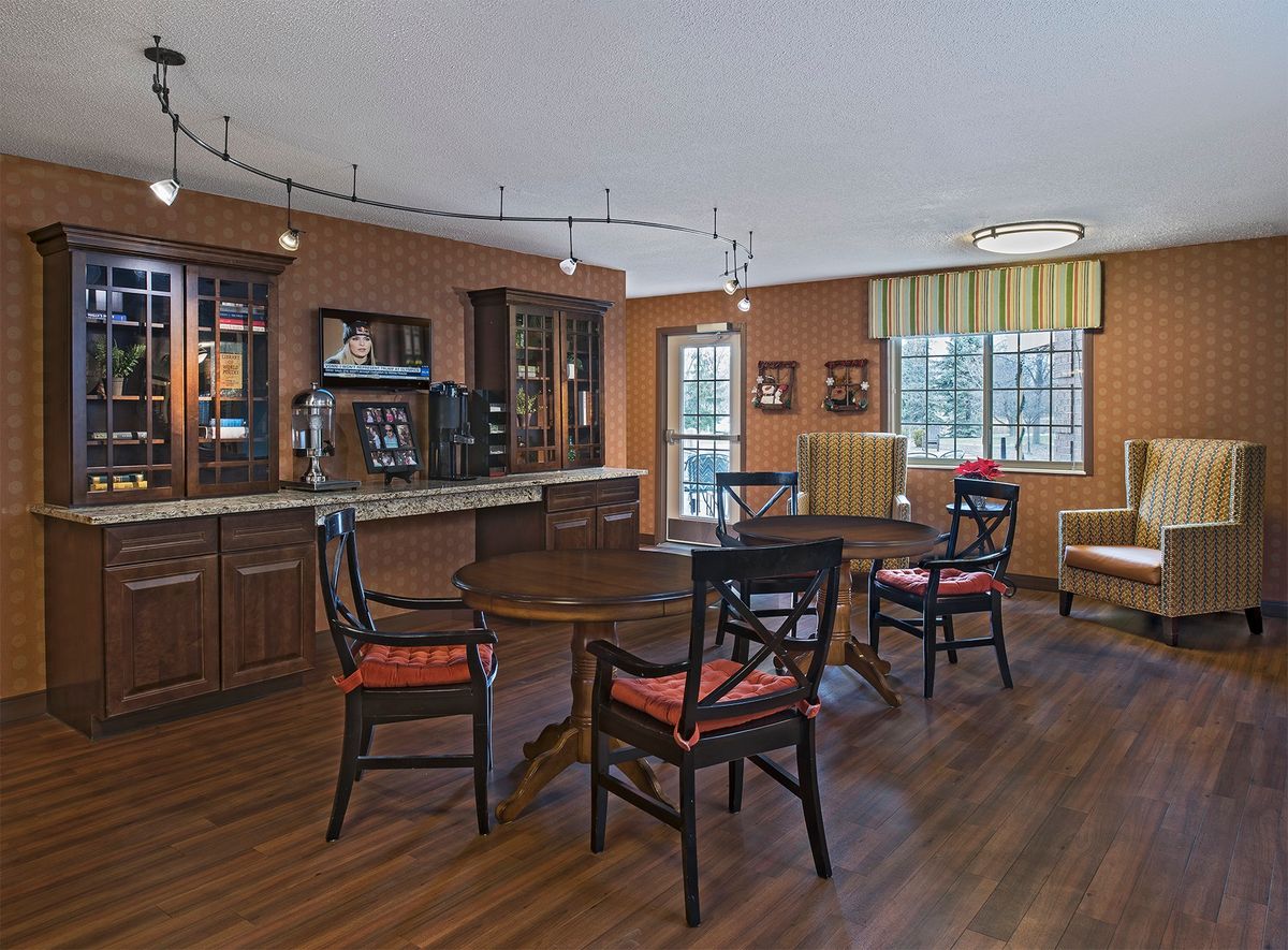 A cozy dining area with wooden flooring, a bar counter, and several tables and chairs.