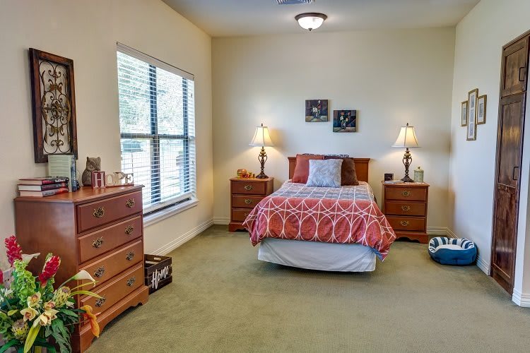 A cozy bedroom with a bed, nightstands, and dressers, featuring warm lighting.