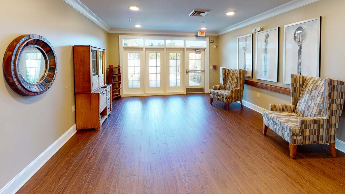A spacious lobby area with wooden flooring, seating, and large windows allowing natural light.