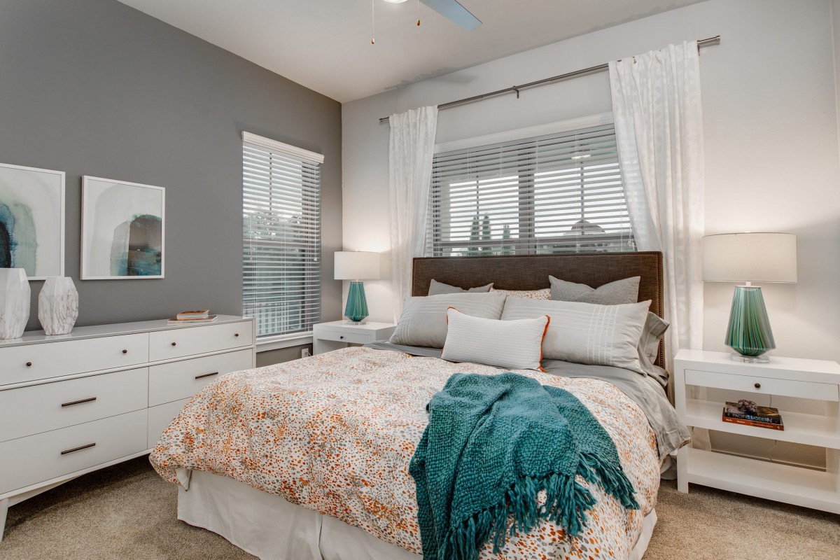 A cozy bedroom featuring a neatly made bed with decorative pillows and a throw blanket, complemented by elegant curtains and soft lighting.