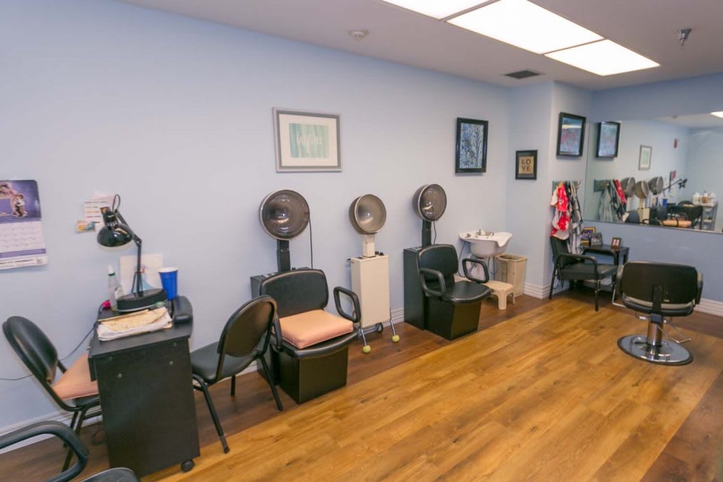 The interior of a hair salon featuring chairs and dryers along the wall with various decorations.