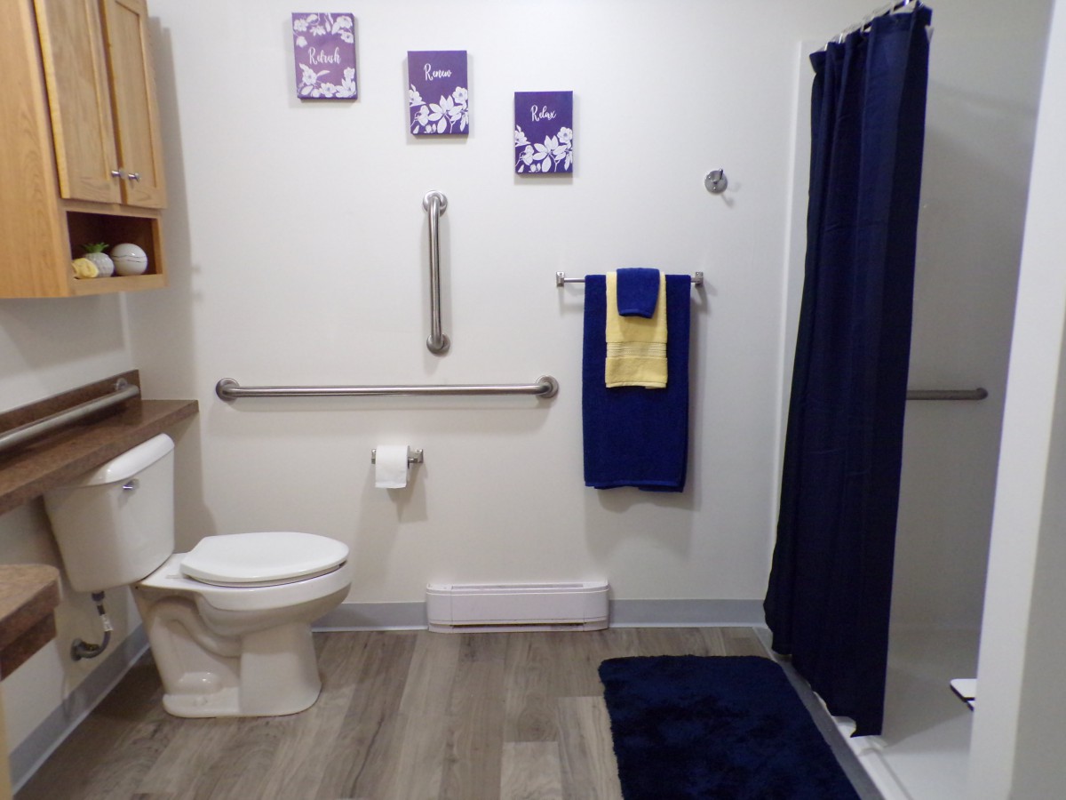 A well-organized bathroom featuring a toilet, grab bar, and navy blue accents including a shower curtain and towels.