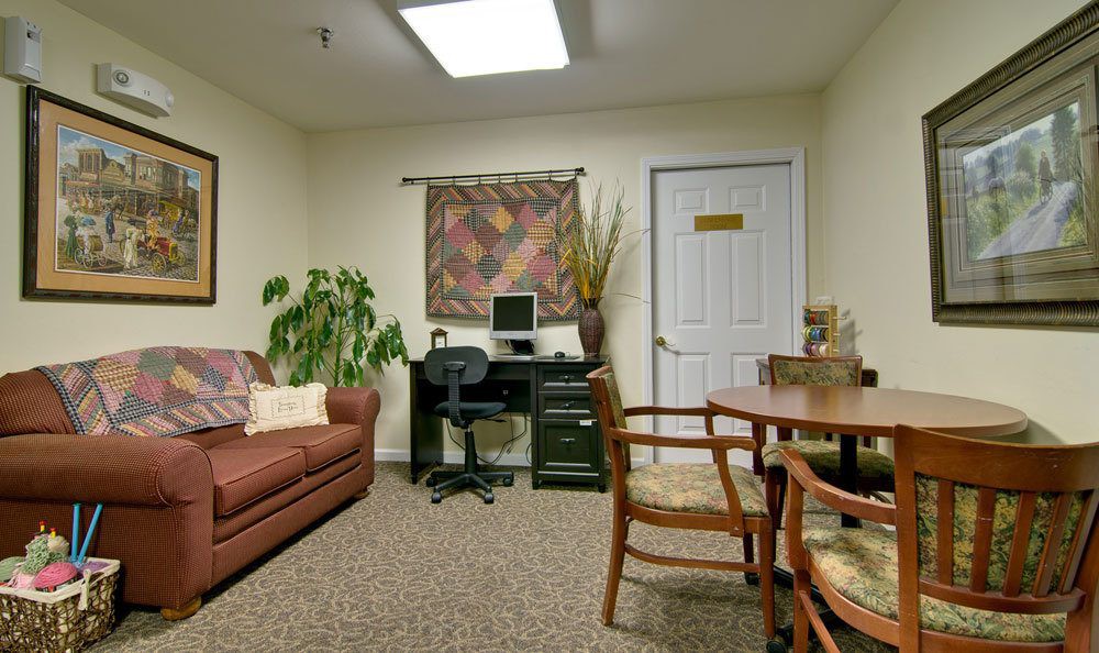 A small office with a sofa, desk, and chairs, featuring a computer and decorative items.