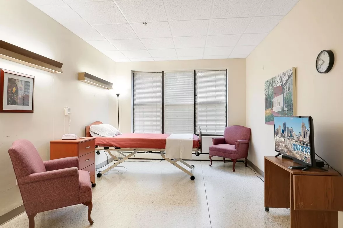 A clean and well-lit hospital room with a single bed and chairs.
