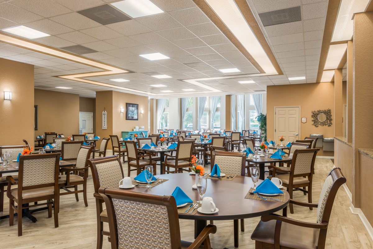 A spacious and elegantly set dining room with neatly arranged tables and chairs, featuring vibrant blue napkins.