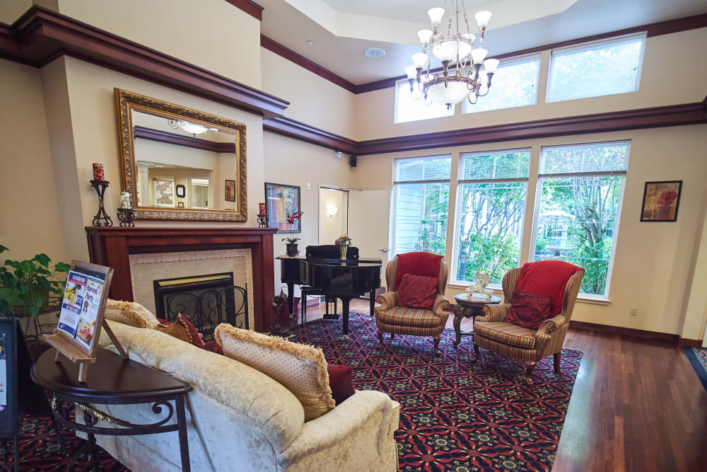 A cozy living room with elegant decor, featuring a grand piano, fireplace, and large windows.