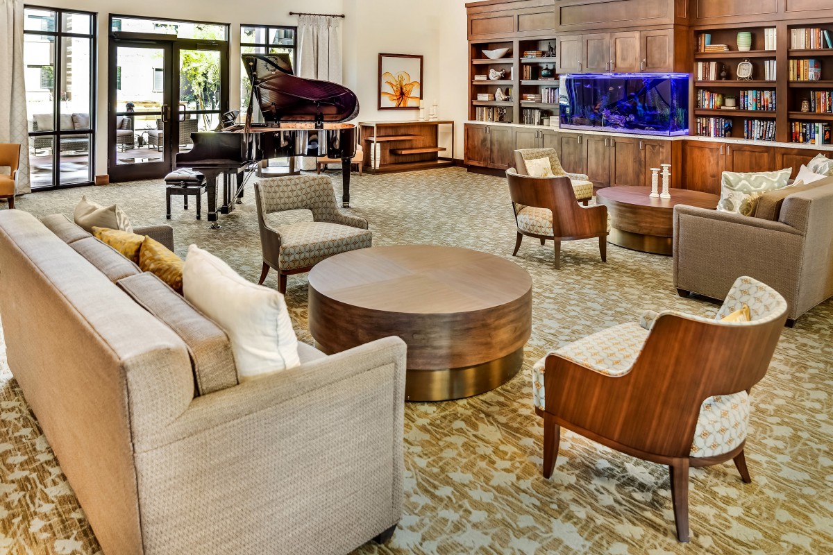 A spacious and elegant living room featuring comfortable seating, a grand piano, bookshelves, and an aquarium.