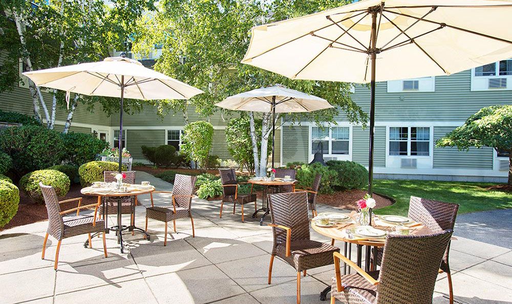 A sunny outdoor patio with tables and chairs under large umbrellas, surrounded by greenery.