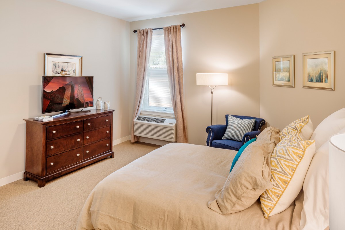 Cozy bedroom with a bed, dresser, and seating area.