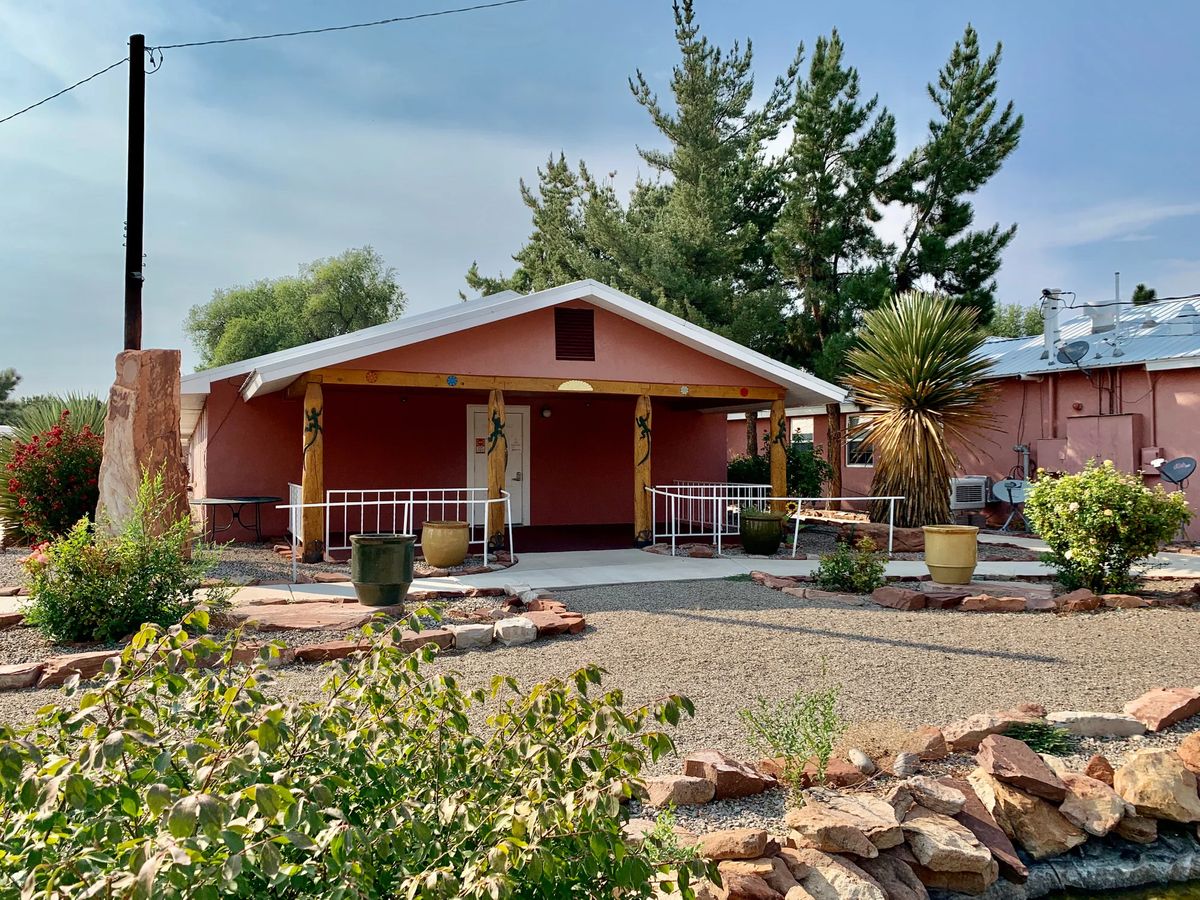 A cozy bungalow with a neatly landscaped front yard and a welcoming porch, set in an arid climate.