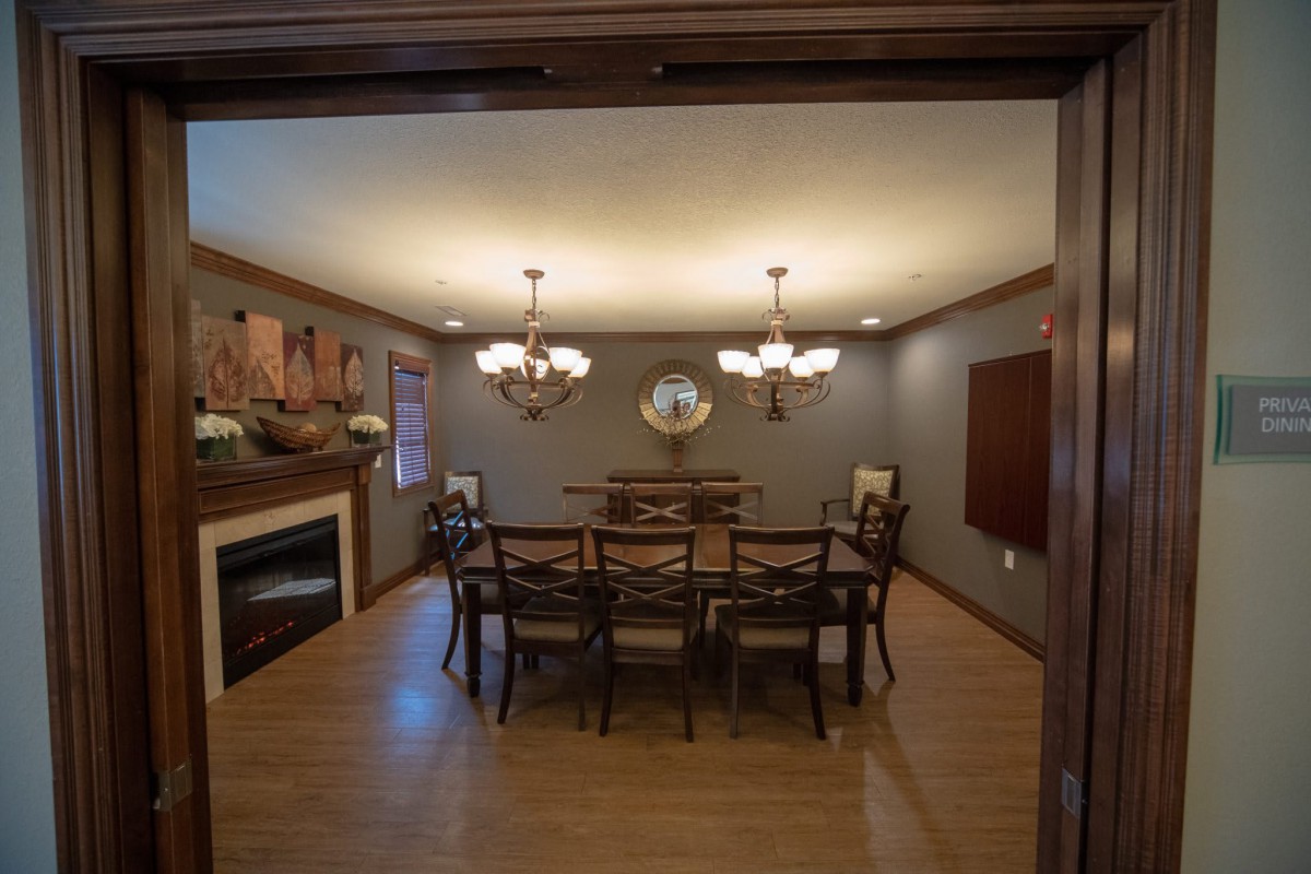 A cozy dining room with a large table, surrounded by chairs, and lit by elegant chandeliers.
