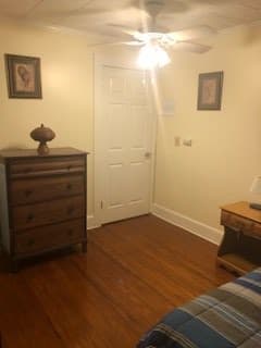 A cozy bedroom with a dresser and a side table, featuring wooden floors and decorative wall art.