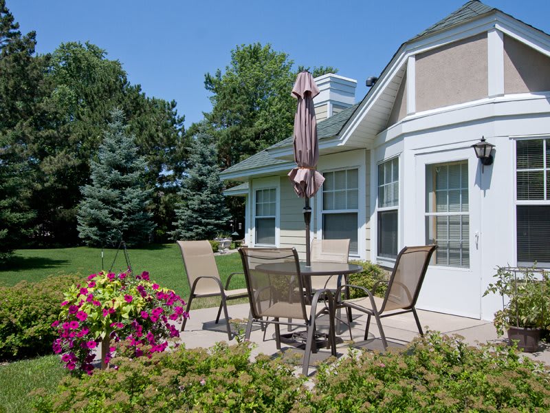 A serene backyard patio with outdoor furniture, surrounded by blooming flowers and a well-kept lawn.