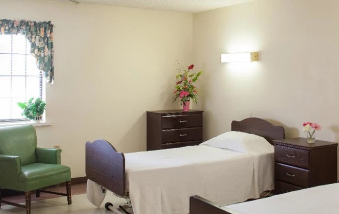 A simple, clean hospital room with two beds and a dresser adorned with flowers.