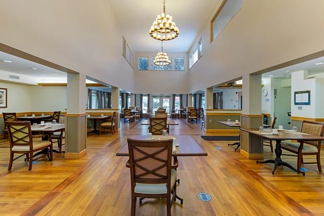 A spacious dining area with wooden floors, elegant chandeliers, and ample natural light.